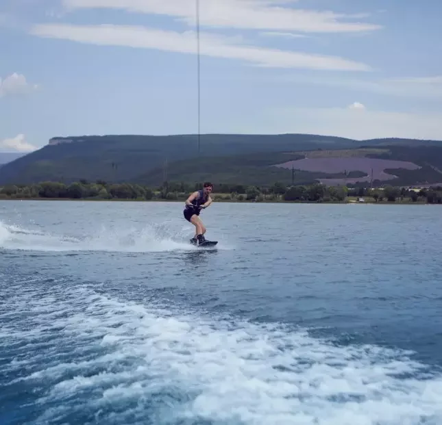 young-sportsman-surfing-across-lake-surfer-wearing-wet-swimsuit-training-wake-park-wakeboarding-river-pulled-by-motor-boat-clinging-cable-wakesurfing-waterskiing-sports-recreation
